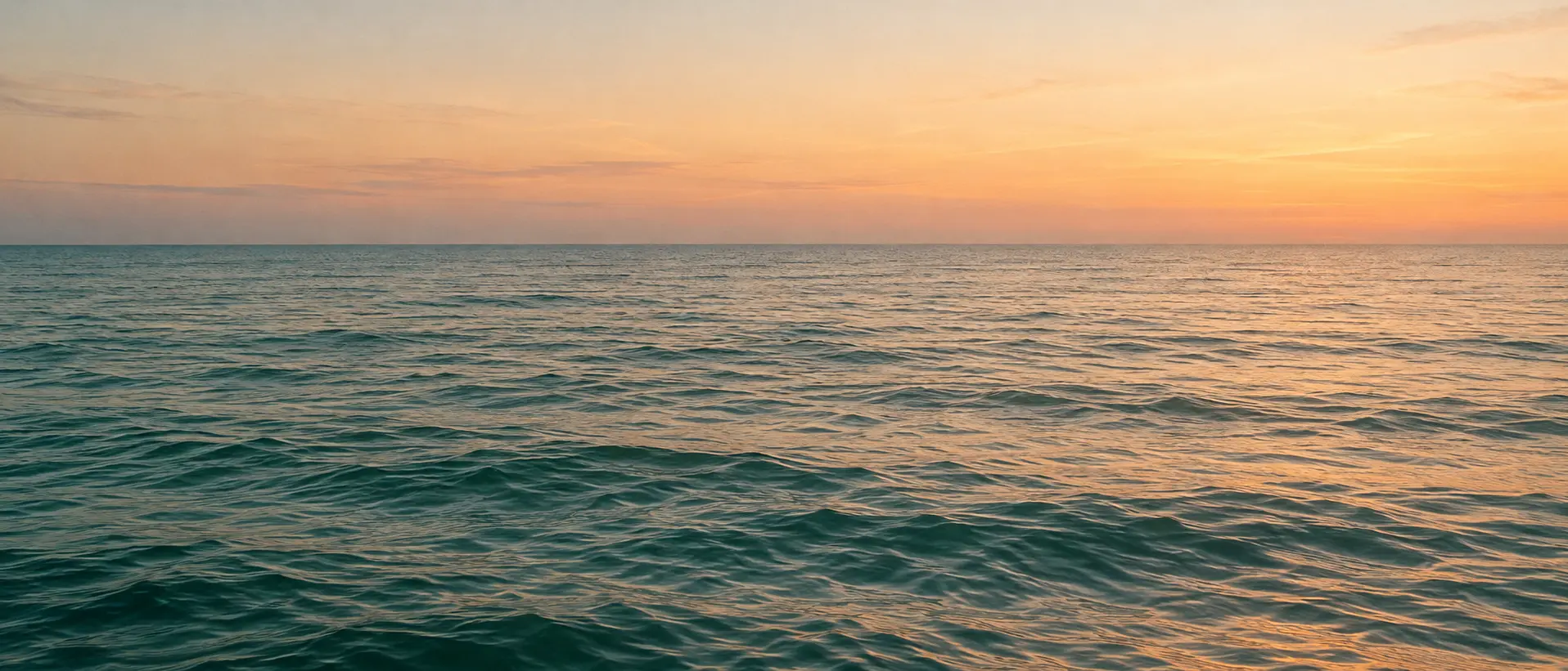 Agua tranquila y un horizonte despejado bajo un cielo de tonos durazno.